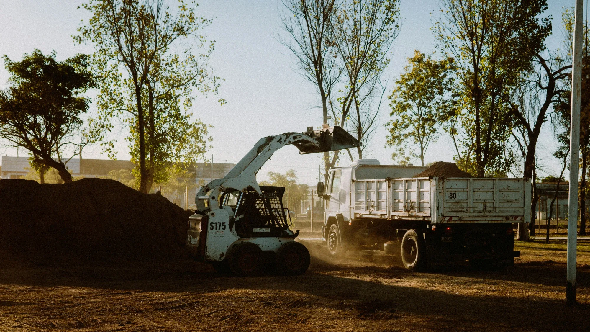 Skid steer loader filling a tip truck with dirt on a work site